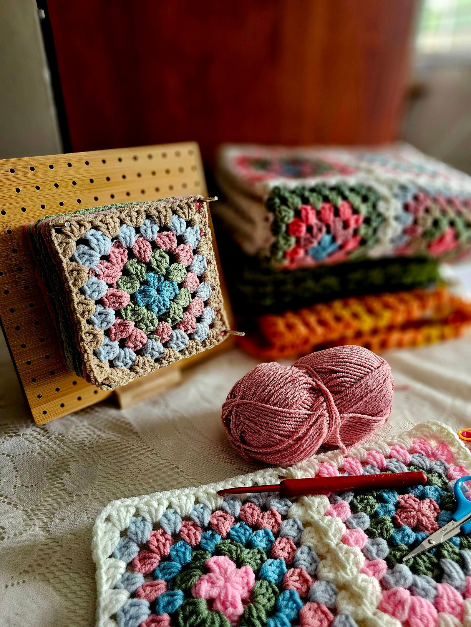 Granny squares, pink yarn and a crochet hook on a cozy table